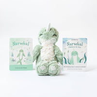 The Slumberkins Seaform Narwhal Kin sitting between the accompanying board book and affirmation card.