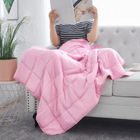 Person reading a magazine on a couch with a pink weighted blanket on their lap