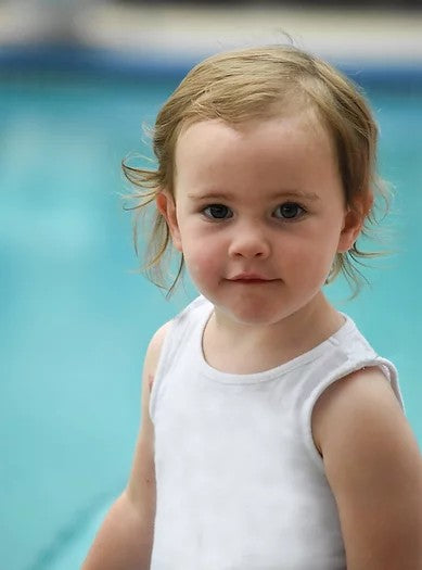 A toddler with fair skin tone and short light brown hair is wearing the white Simply Sleeveless Sensory Compression Shirt.