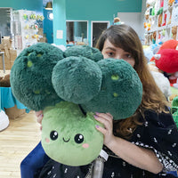 A person with light skin tone and long brown is partially obscured by the size of the Comfort Food Broccoli Squishable.