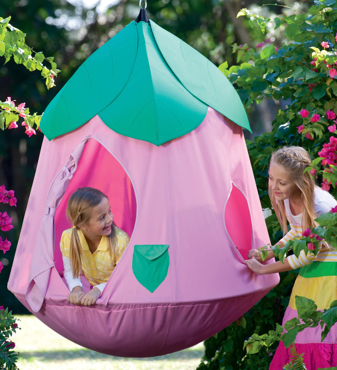 The CozyPosy HugglePod hangs in a yard. One child is looking out of the open door while another peers in through a side window.