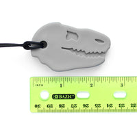 A grey Dino-Bite Chew Necklace sits next to a ruler showing the length of the pendant at 2.5".