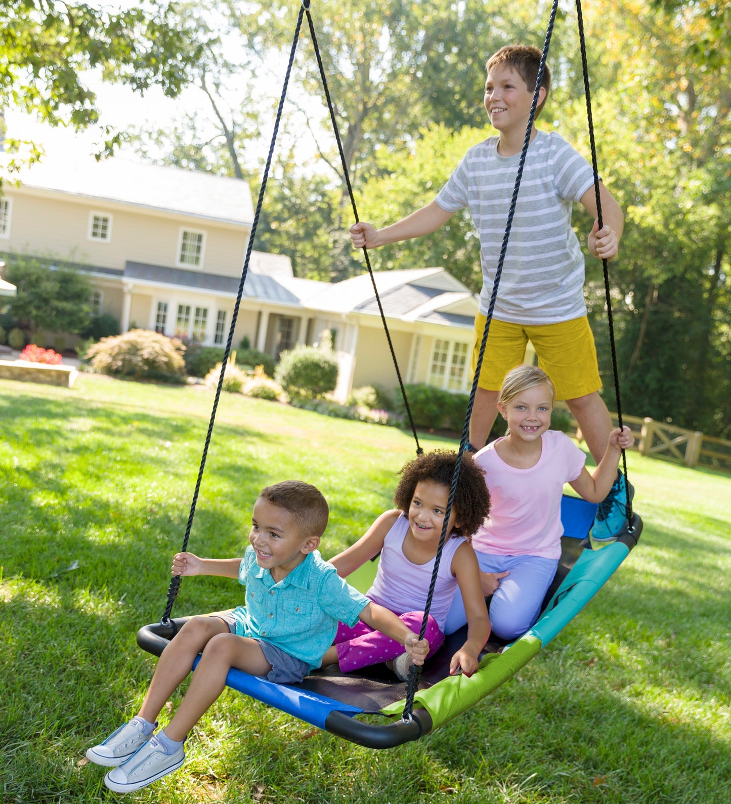 Three children sit on the Colorful Super Platform Swing and one stands at the rear. They are all smiling and looking in the same direction.