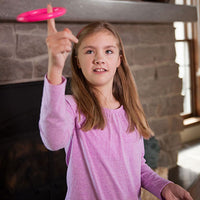 A child with light skin tone and long brown hair is holding an arm up bent at the elbow. Their pointer finger is extended and is balancing a pink ring that is spinning around it.