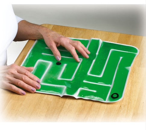 An adult sits at a table with the Gel-Maze with Marbles in front of them. They are moving the marble through the maze with their left hand.