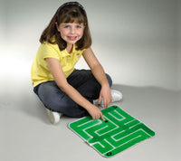 A child with light skin tone and shoulder length brown hair is sitting criss cross applesauce on the floor in front of the Gel-Maze with Marbles. They are pointing to the marble in the maze.