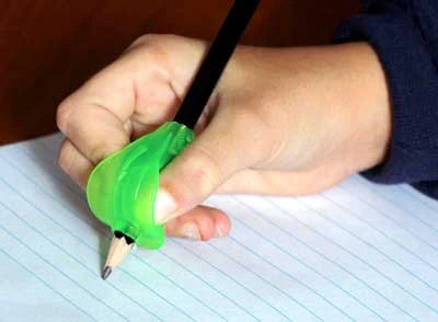 A hand with light skin tone holds a lime green Grotto Grip fitted around a pencil up to a piece of lined paper.