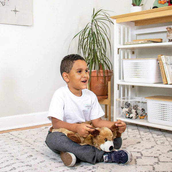 A child with medium skin tone and short black hair is sitting with their legs crossed and the Weighted Lap Dog on their lap.