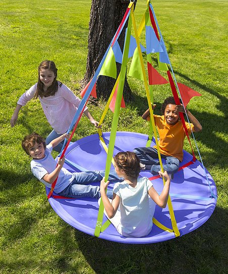 Three children sit across from each other on the Rainbow Flag Swing while one child pulls the swing.