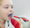 A child with light skin tone has their mouth open. A gloved hand holds a Z-Vibe and presses it against their tongue.