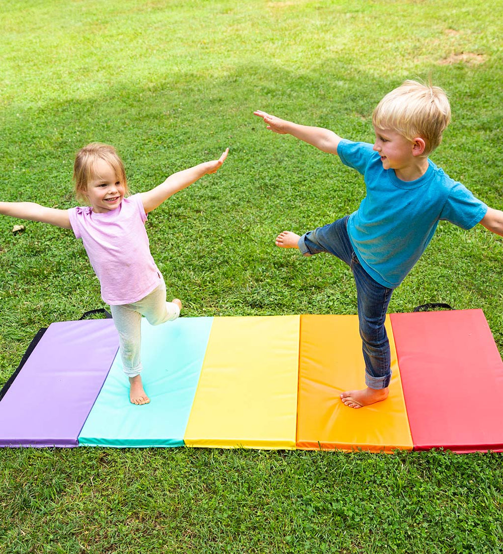 Two children are doing an acrobatics pose on a colorful Tumbling Mat. They are in a yard outside.