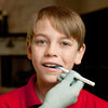 A child with light skin tone and short brown hair opens their mouth. A gloved hand holds up an Oral Motor Probe whose tip is in their mouth.
