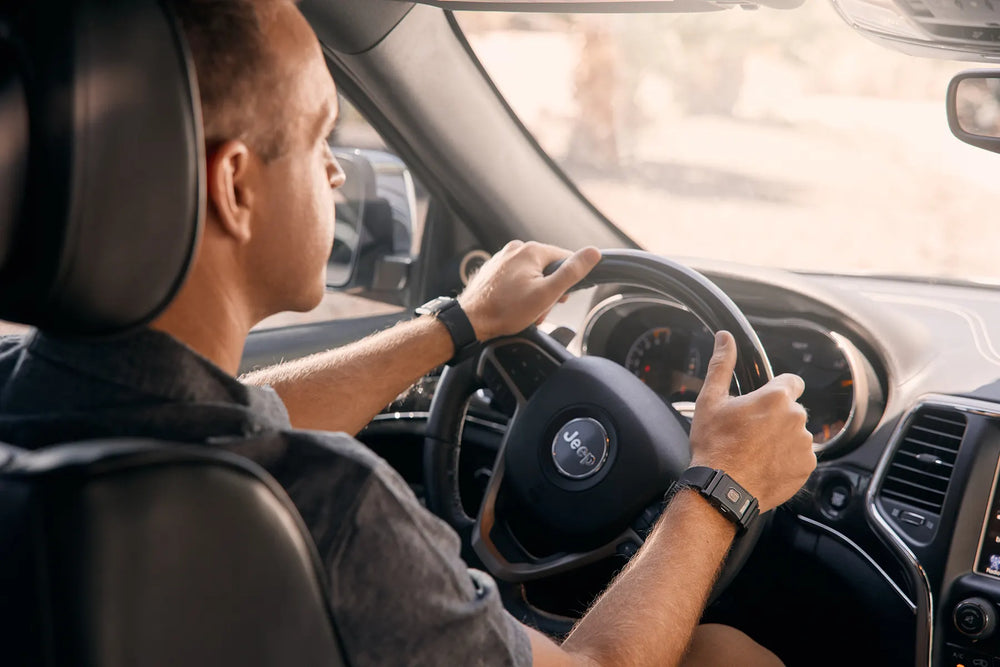 A person with light skin tone and short brown hair is sitting behind a wheel with their hands on it. They are wearing the TouchPoints with Wristbands.