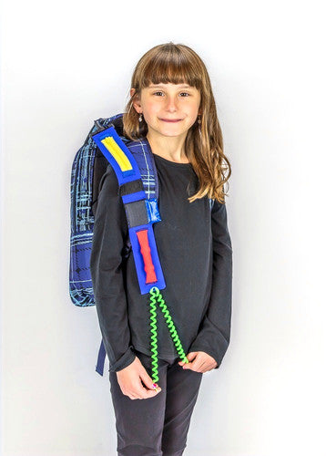 A child with light skin tone and long brown hair wears a backpage with a Sensory Seeker Clip On attached to it. They are pulling on the green spirals at the bottom of the Clip On.