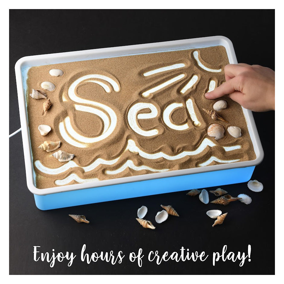 A child with light skin tone draws the text "Sea" with a sun and waves into a sand table.