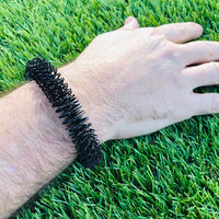A hand with light skin tone rests on some grass while wearing a black Wrist Spikey.