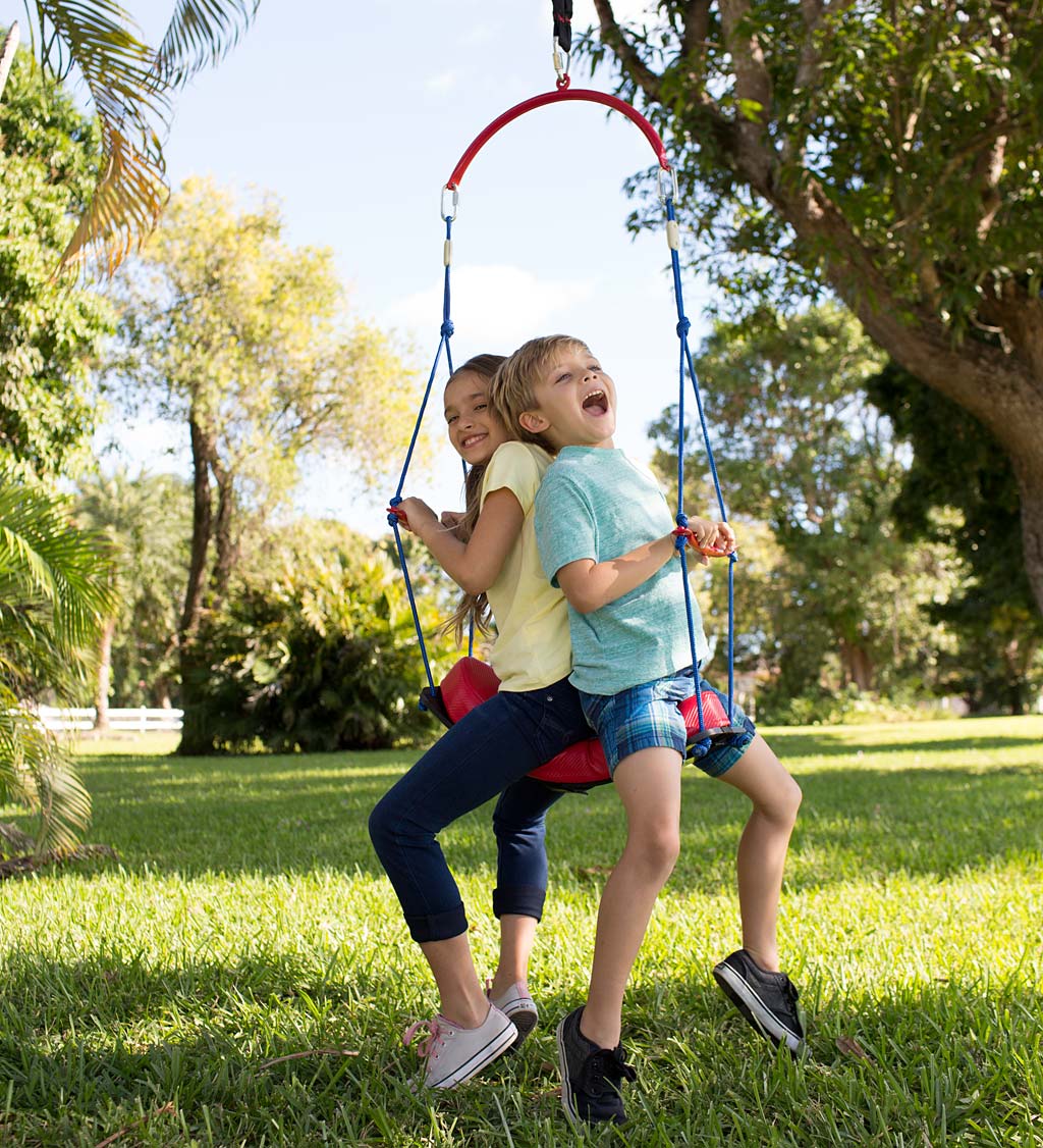Two children sit back to back on the BungeeBounce Swing. They are holding onto the side bar and smiling while they dangle.