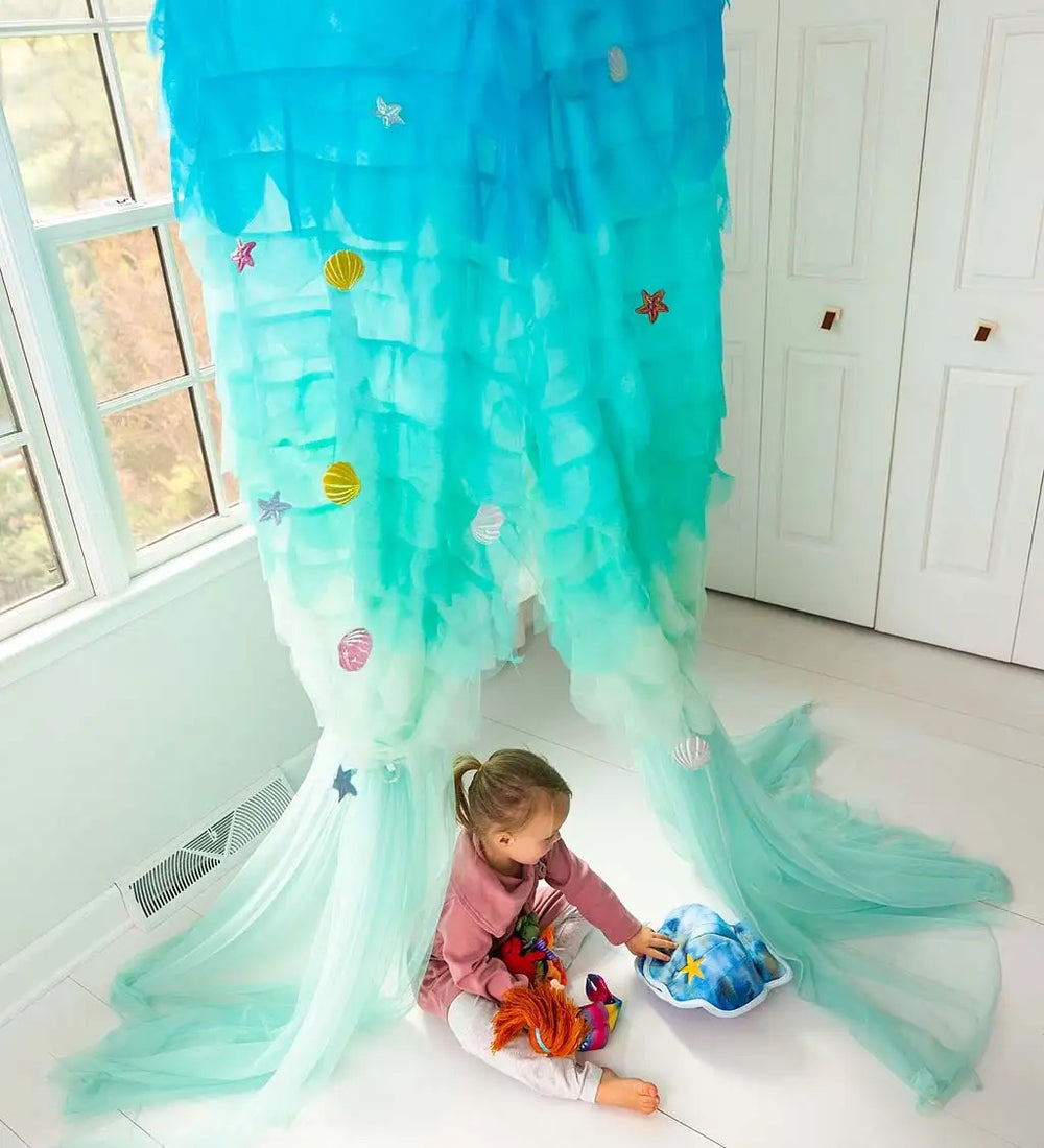 A child sits underneath the Light-Up Mermaid Canopy with several other toys. 