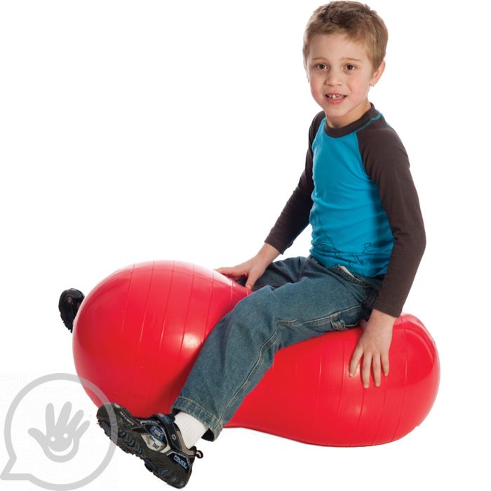 A child with light skin tone and short brown hair straddles a red Peanut Ball.