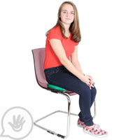 A teenager with light skin tone and long brown hair sits on the Teen Gel Cushion, which is sitting on top of a chair.
