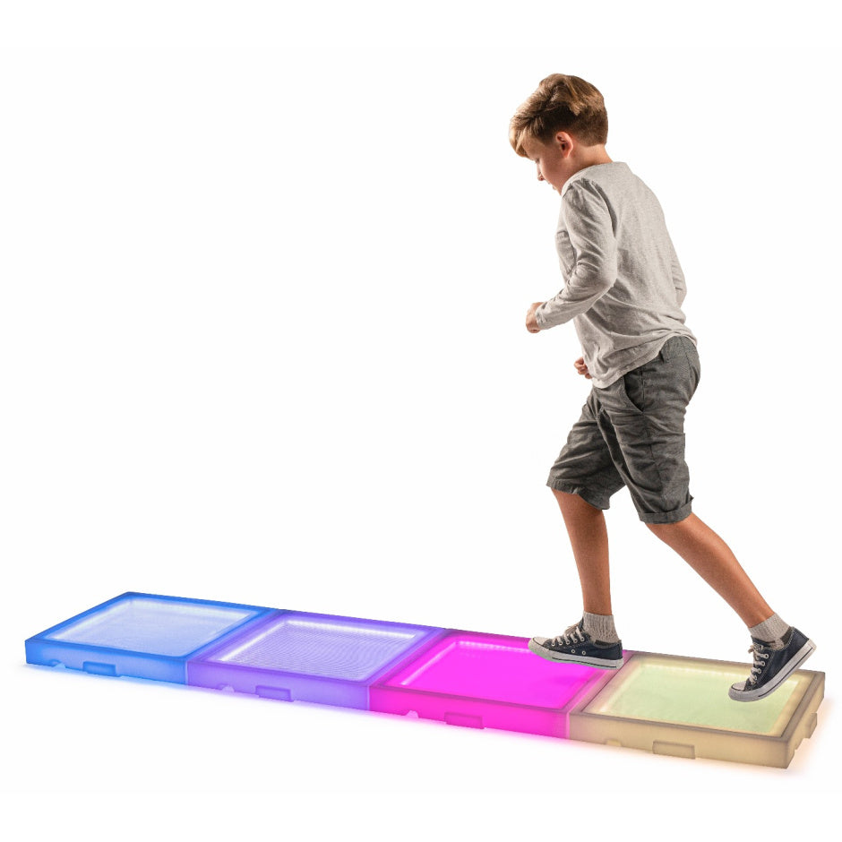 A child with light skin tone and short blonde hair runs across four lit up colorful tiles.