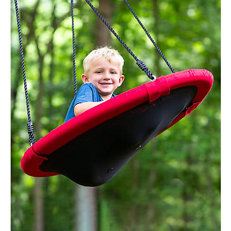 A child with light skin tone and short light blonde hair is leaning forward while flying through the air on a Sensory Snuggle Oval Swing. They are smiling and you can see the bottom of the swing, with its hug-like effect.