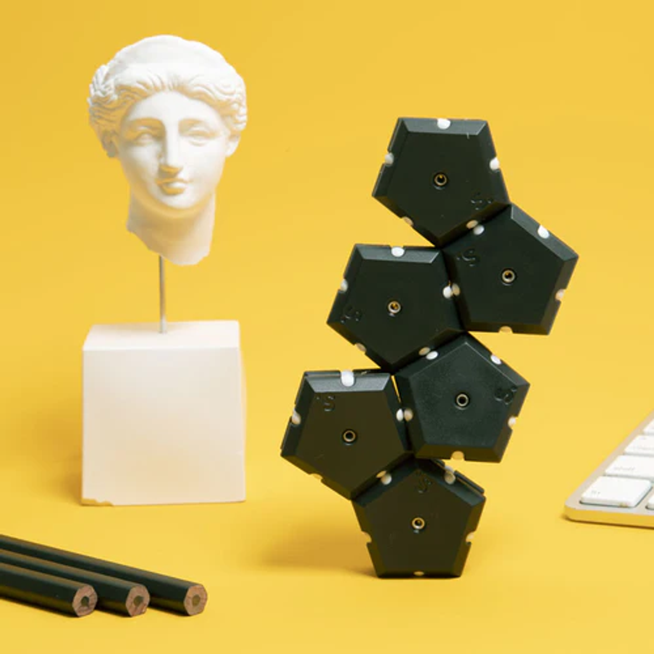 The Snake Eyes Geode Pop forms a small structure standing independently, next to three unsharpened pencils and a sculpture in the shape of a Roman head.