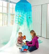 Two children sit underneath the Light-Up Mermaid Canopy in the corner of a room. They are playing with two dolls.