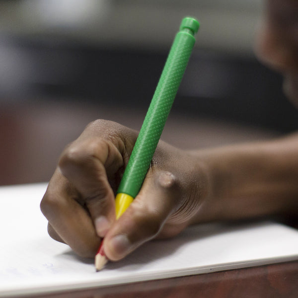 A child with dark skin tone holds a Tran-Quill Vibrating Pencil in their hand.