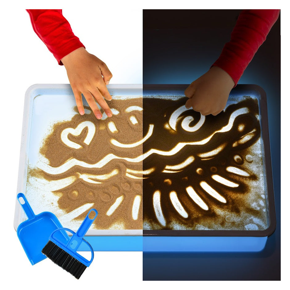 A child with medium light skin tone draws shapes into sand on a lit up sand table. There is a small dust pan and brush in the corner of the image.