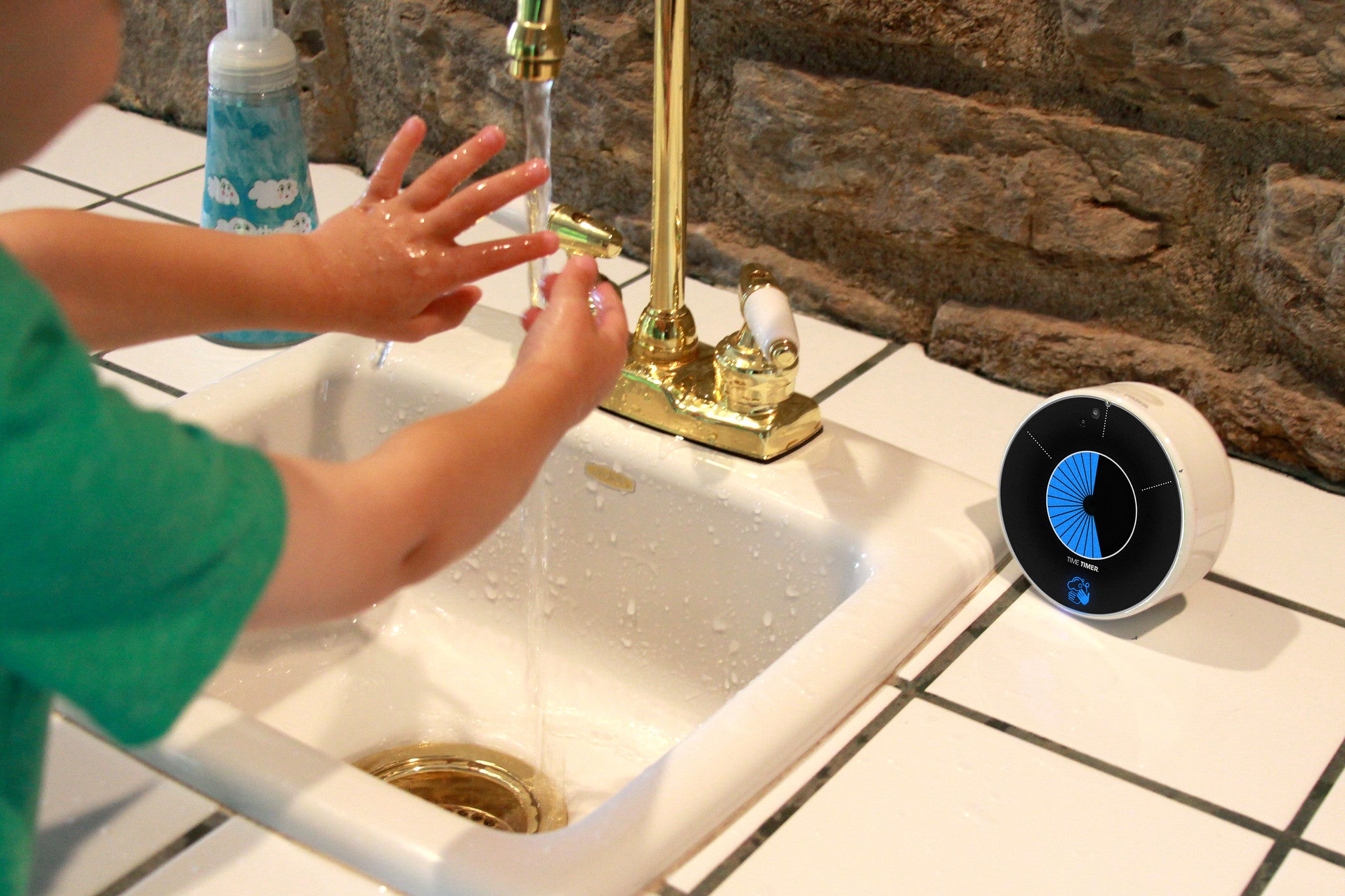 A child with light skin tone stands at a sink with their hands under running water. The Time Timer WASH sits to the right of the sink.