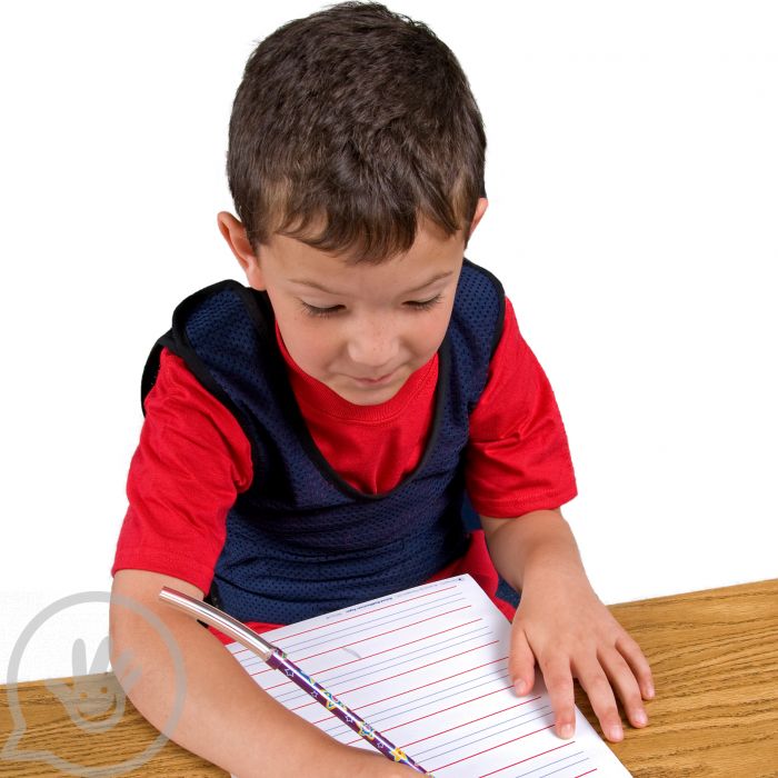 A child with light skin tone and short brown hair sits at a desk and writes with the pencil part of the Pencil Jaw.