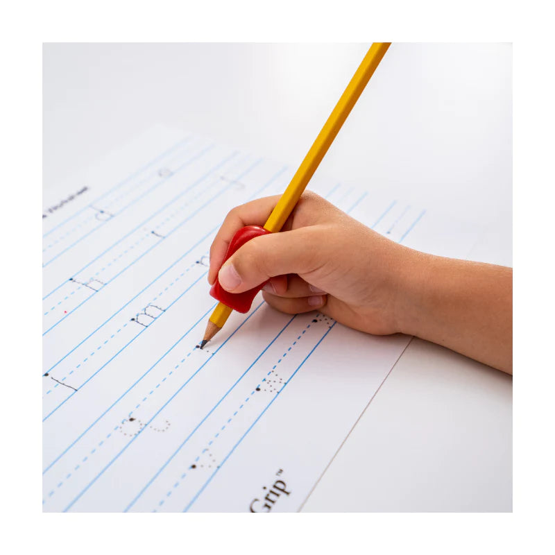 A child's hand with light skin tone holds a red Pencil Grip over a pencil up to a paper where they are practicing writing letters.