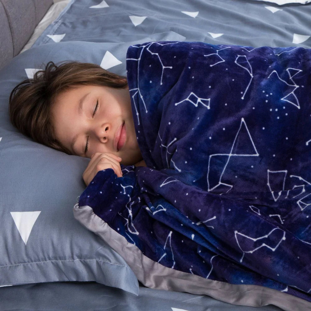 A child with light skin tone and short brown hair is laying on a pillow with the Weighted Blanket for Kids pulled up to their chin.