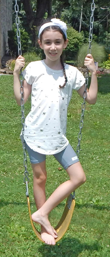 A child with light skin tone and long braided brown hair is standing on a swing. They are wearing a pair of gray Unisex Sensory Compression Shorts.